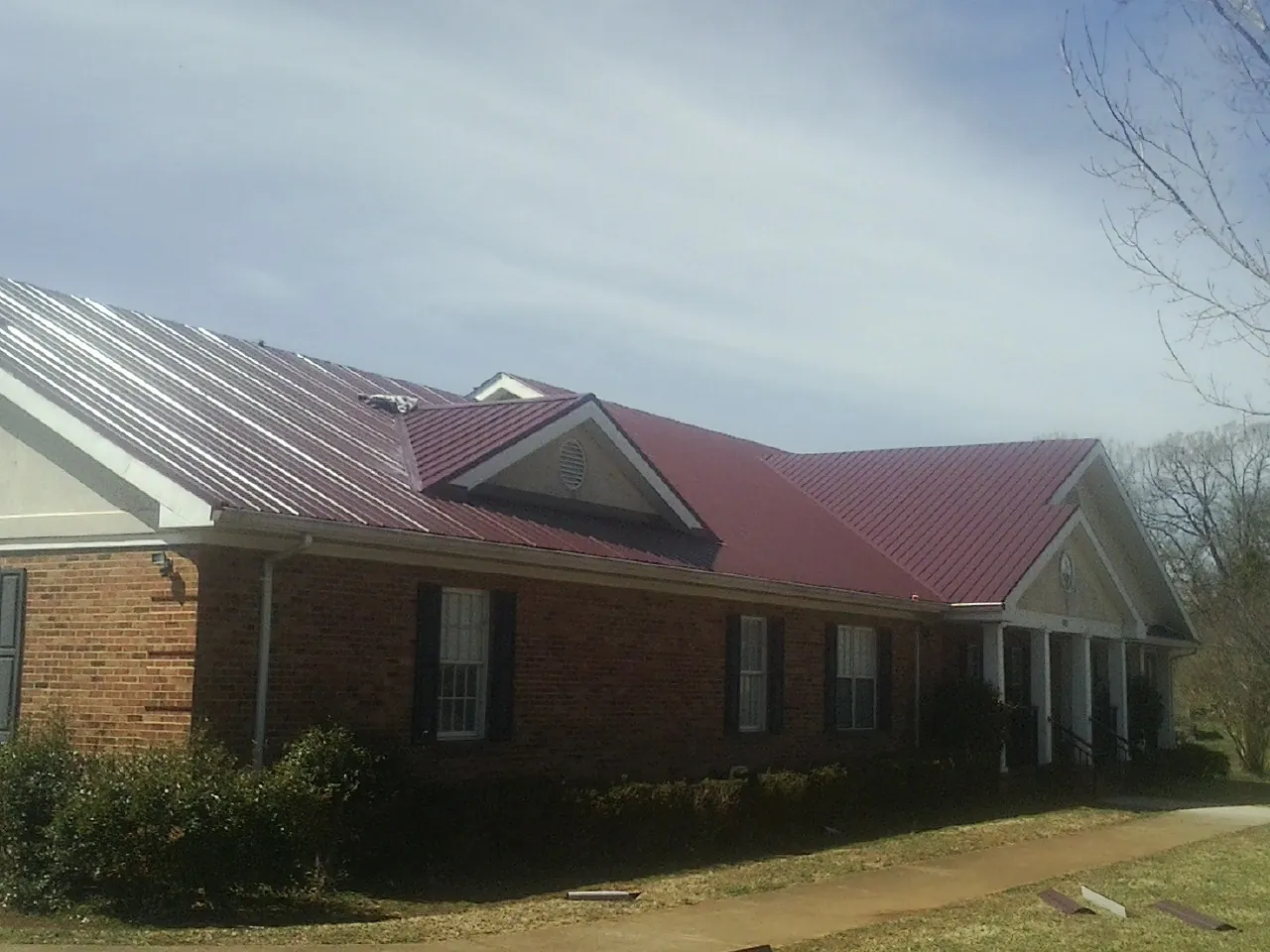 Red metal roof with gabled entries on a long brick building, from a Hail Damage Roof Repair job in Warner Springs